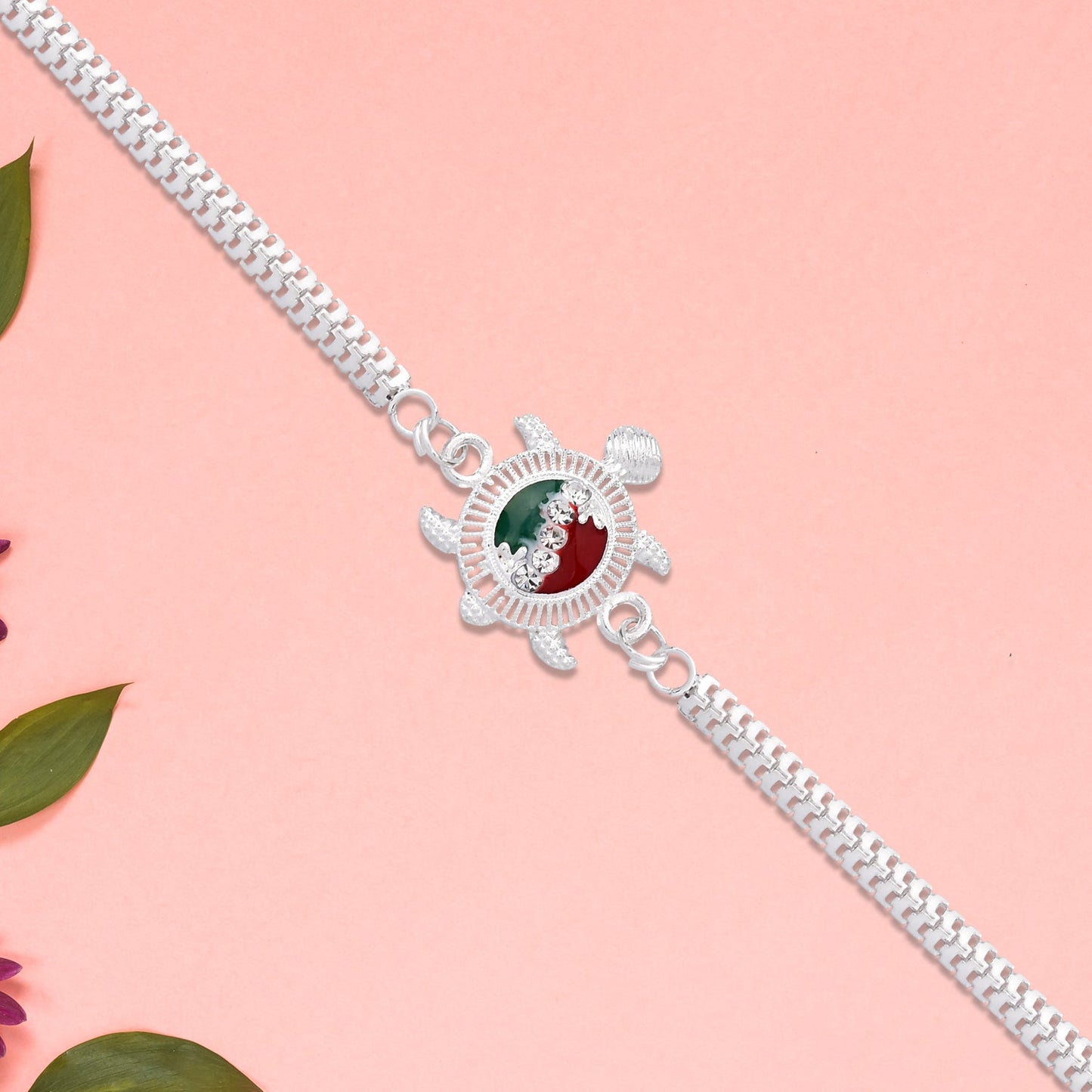 Close-up of handcrafted Turtle Rakhi showing intricate red and green enamel work on silver chain.