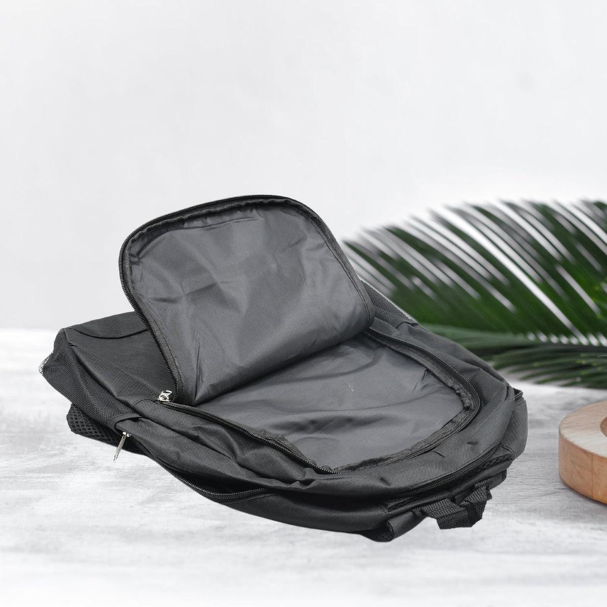 A black fabric backpack with its main compartment open, revealing a spacious interior, rests on a light gray surface with a