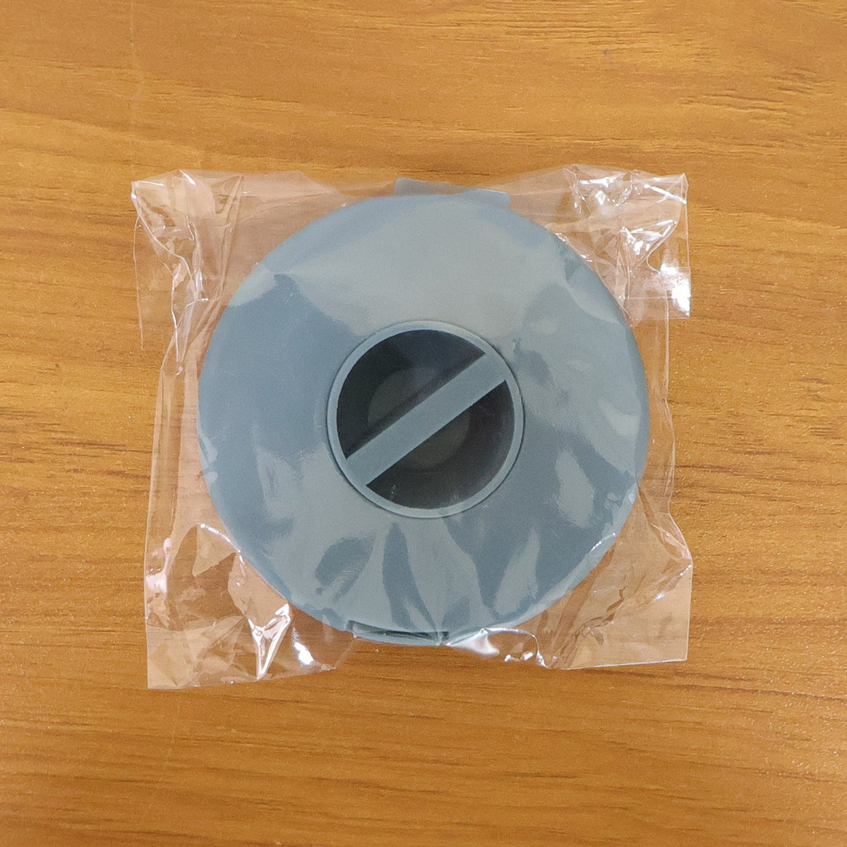 A closed blue cable winder case is sealed inside clear plastic packaging on a wooden surface.
