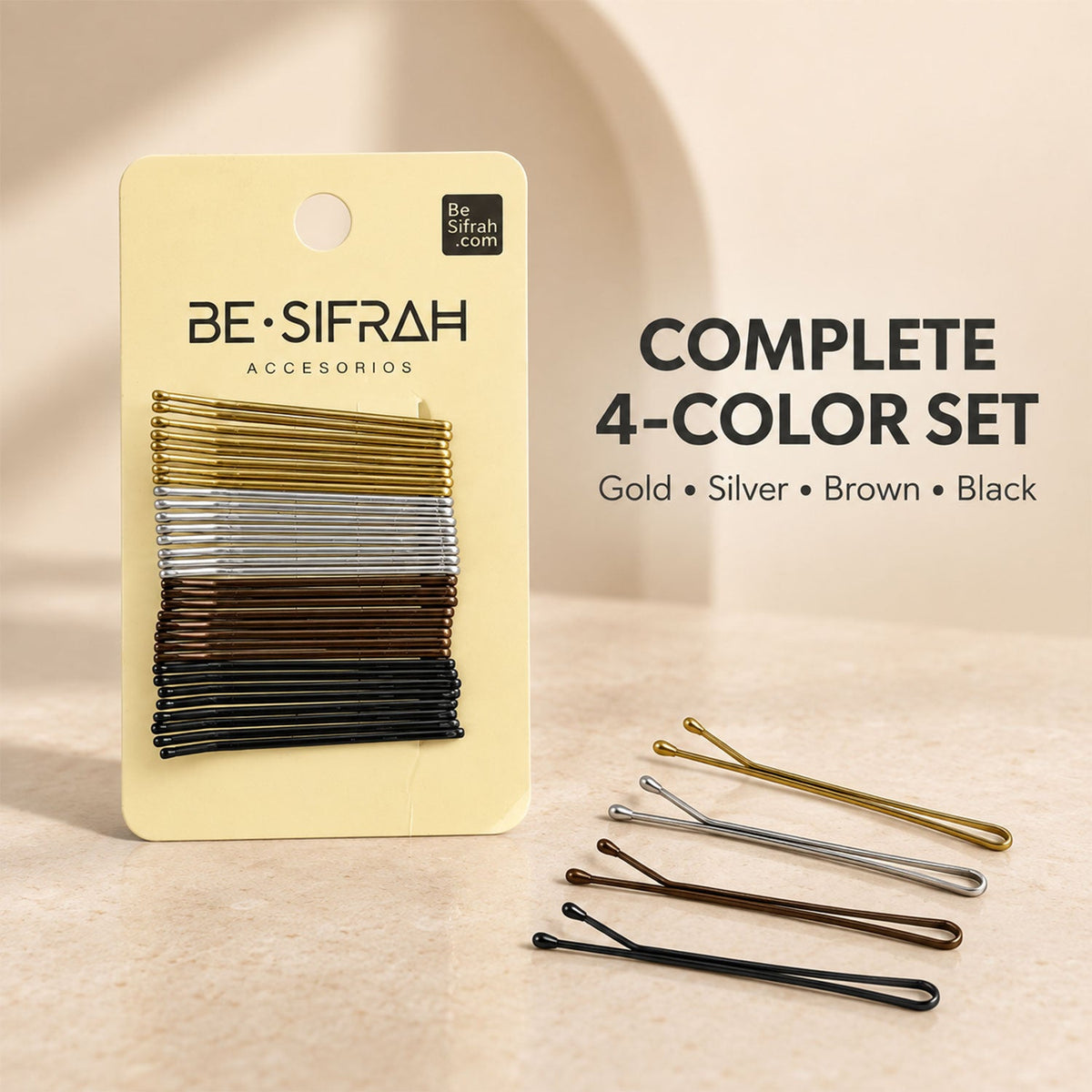 A yellow card of bobby pins is shown with four loose pins in gold, silver, brown, and black on a light surface.