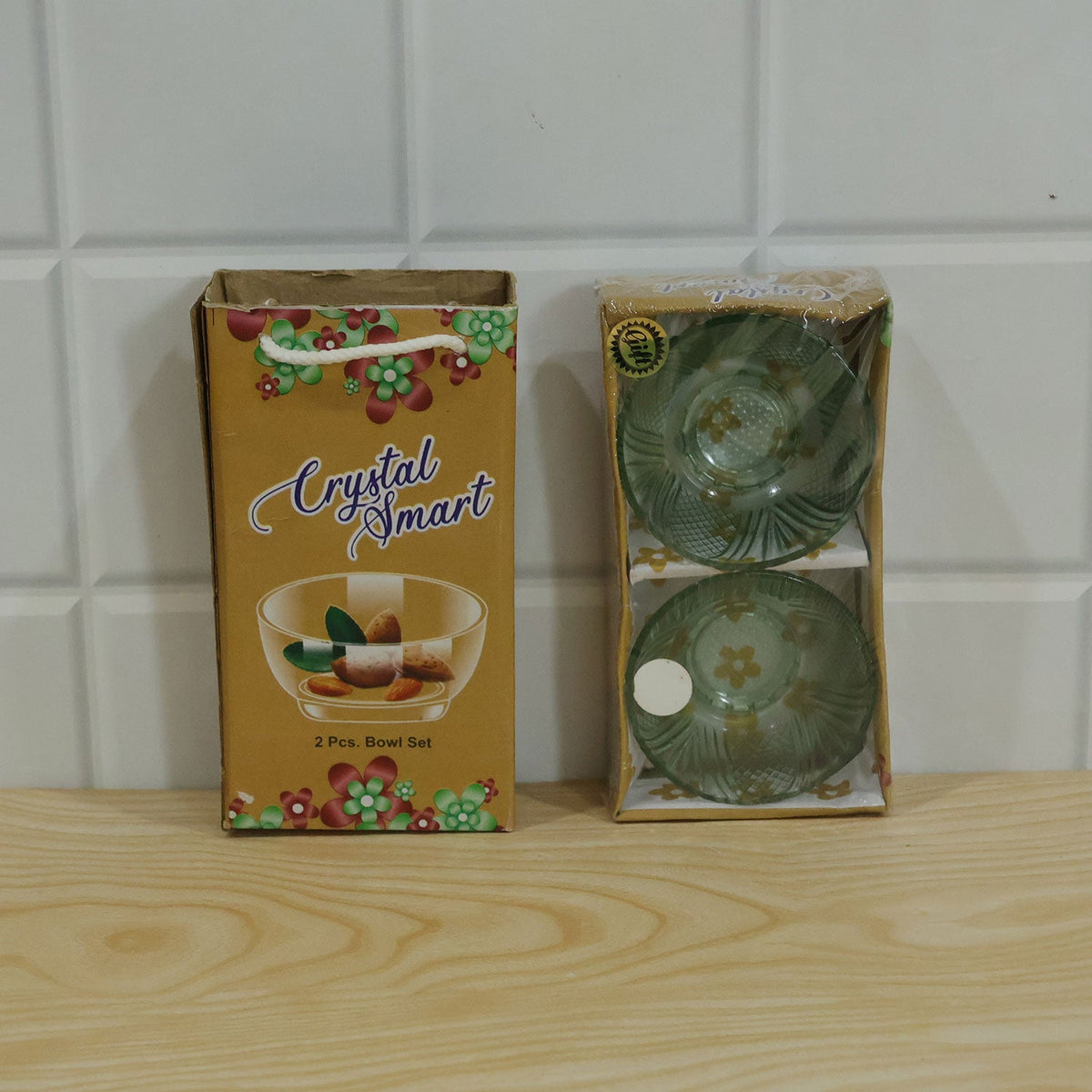 A yellow box containing two green glass bowls, placed on a light wooden surface against a white tiled wall.