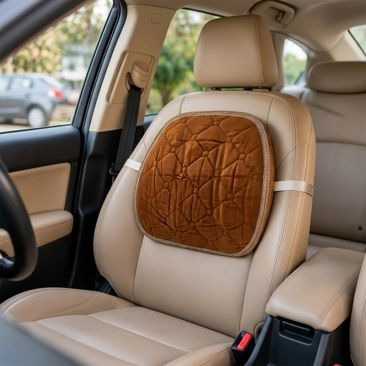 Brown quilted velvet lumbar support cushion strapped to a tan leather car seat in a vehicle.