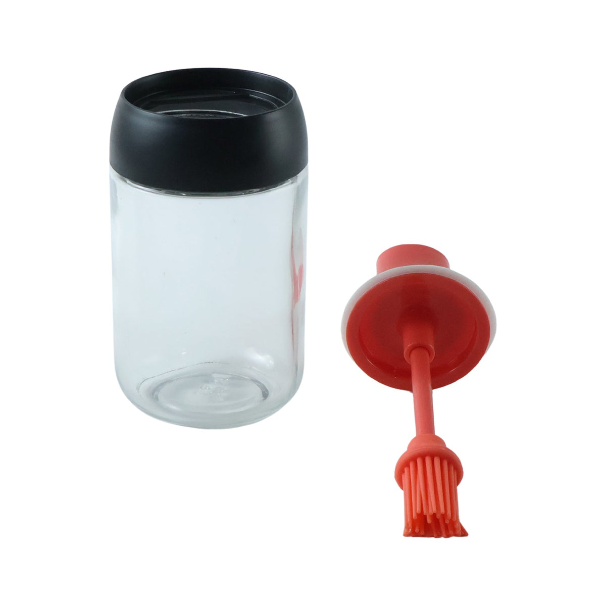 A clear glass oil dispenser with a black top and a detached red silicone brush on a white background.