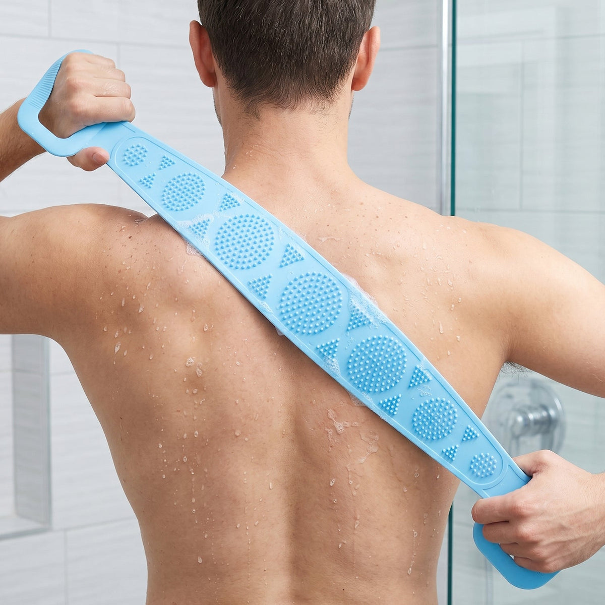 A person uses a blue silicone back scrubber with two handles to wash their back in a shower.