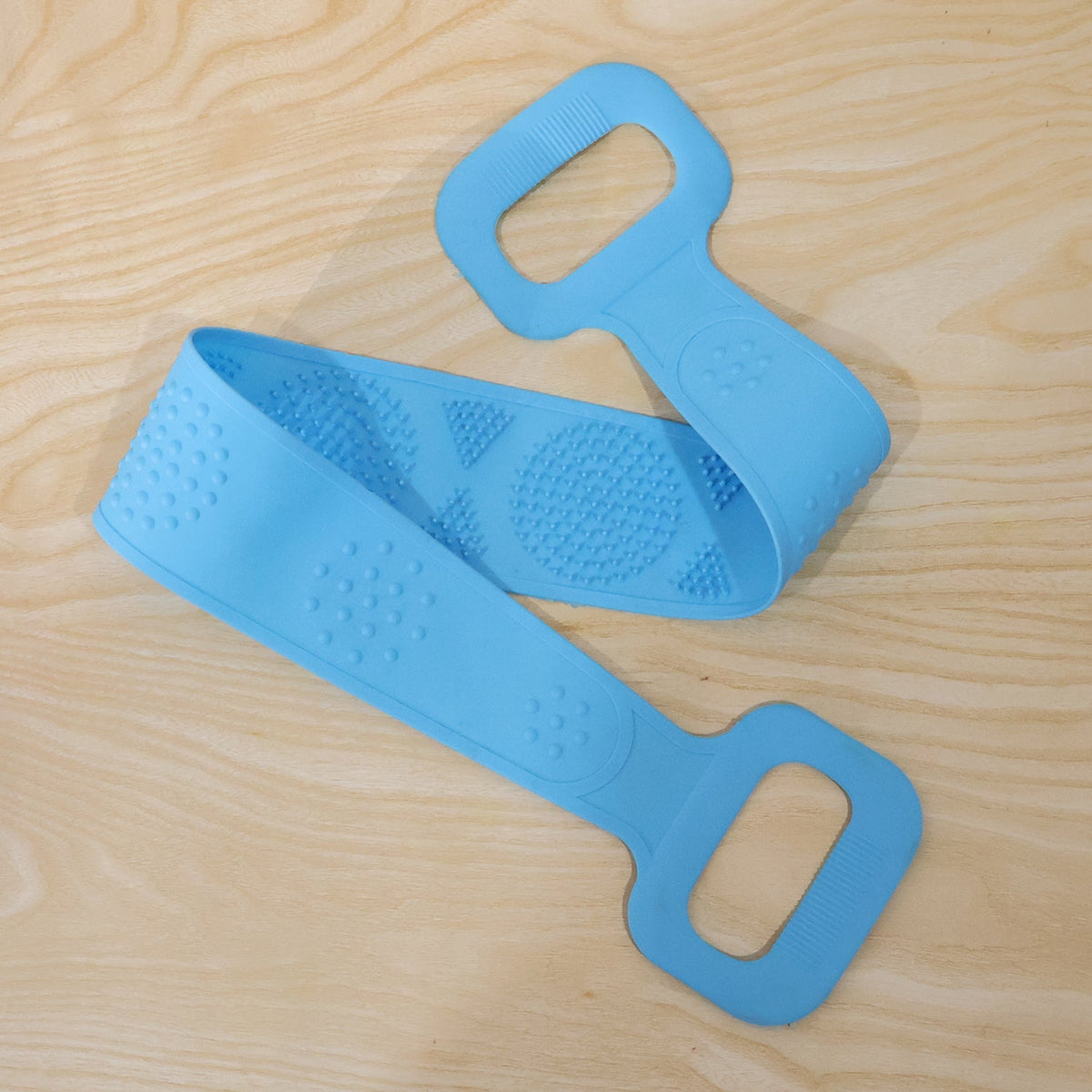A light blue silicone back scrubber with textured surfaces is coiled on a wooden surface.