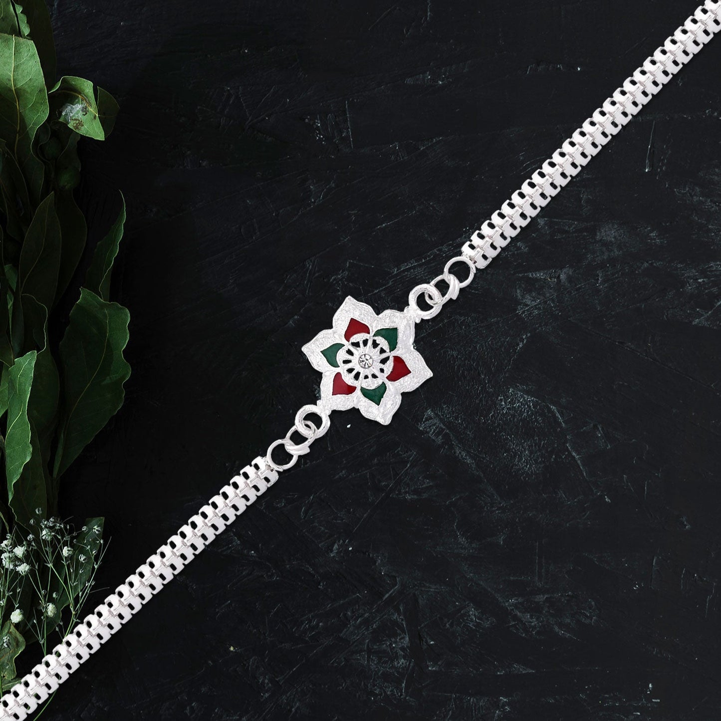 Close-up of Silver Flower Rakhi on wrist showcasing vibrant red and green enamel detailing