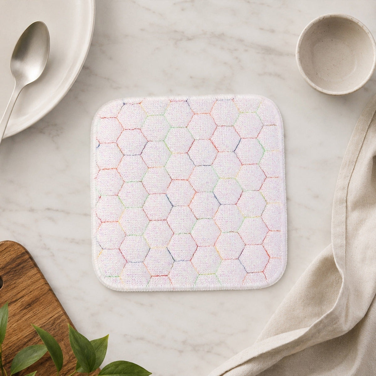 White honeycomb-patterned cleaning cloth on a marble countertop with a plate, spoon, bowl, and linen napkin.