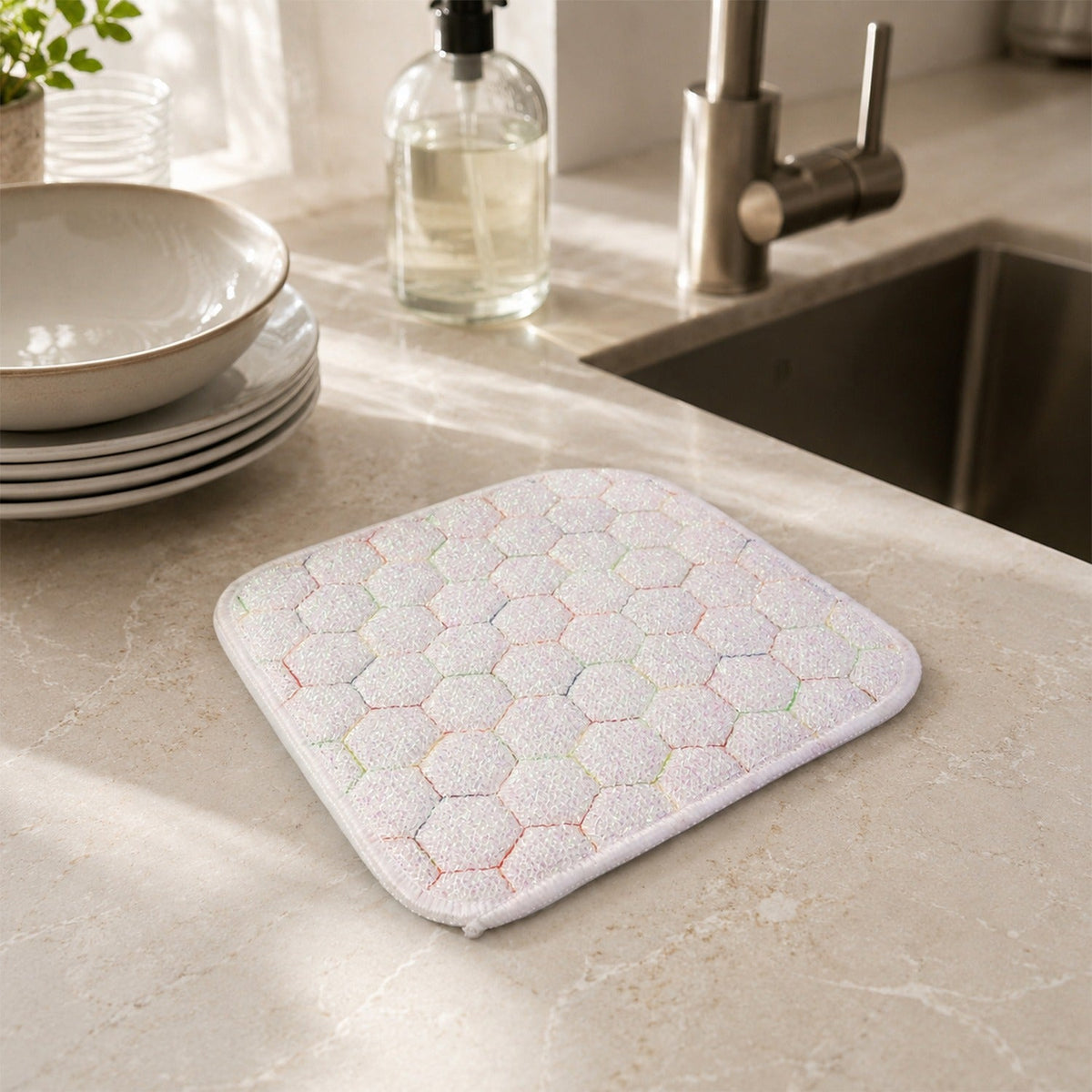 White honeycomb-patterned cleaning cloth on a kitchen counter with a sink, faucet, soap dispenser, and stacked dishes.