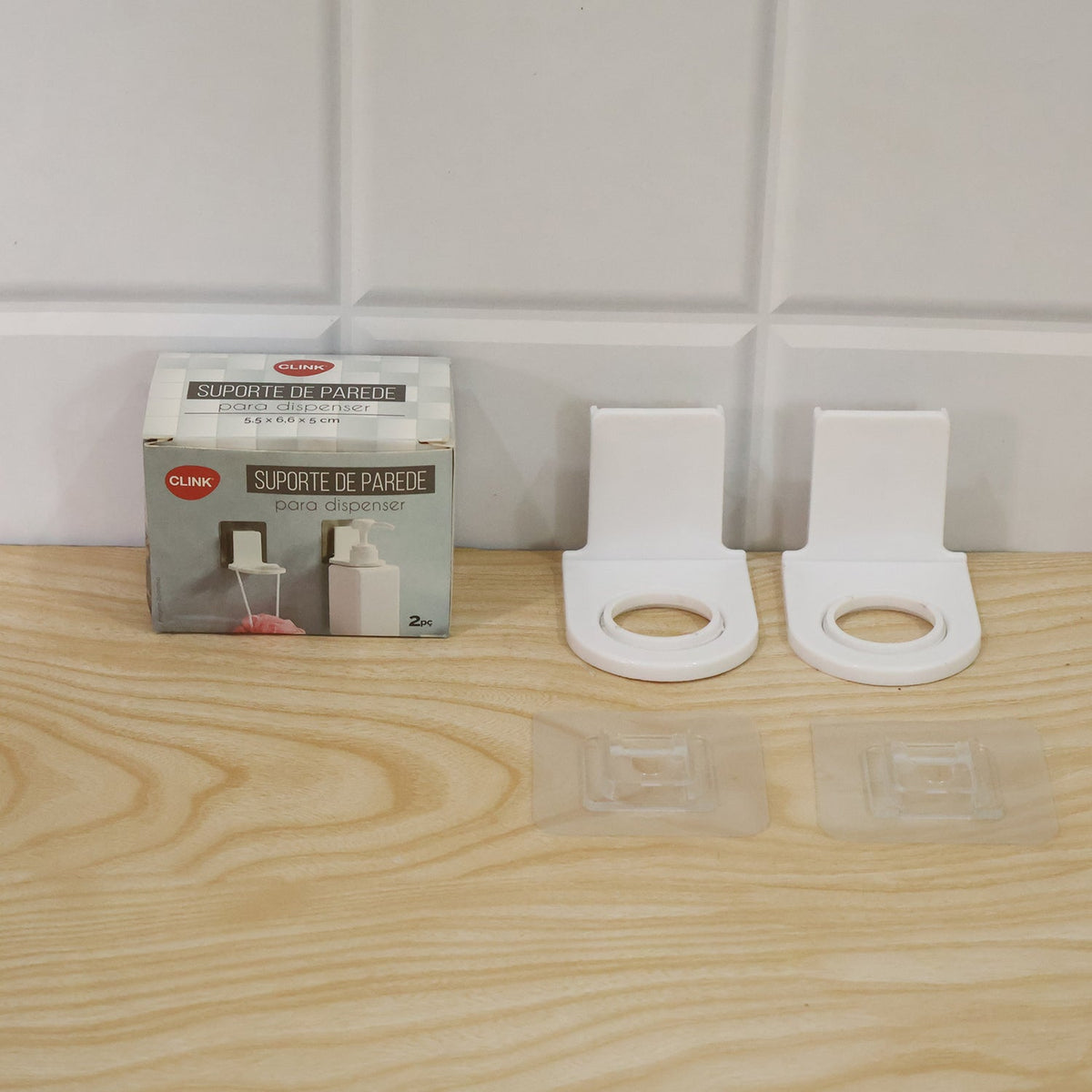 A product box and two white plastic bottle holders with their clear adhesive pads are arranged on a light wooden surface.