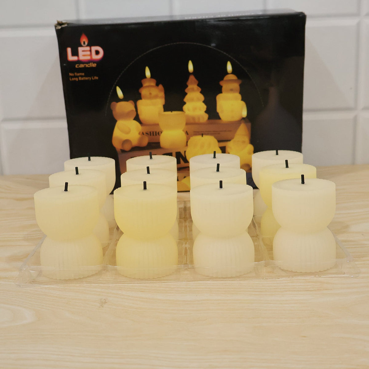 Twelve unlit, cream-colored, ribbed, hourglass-shaped LED candles are displayed in a clear plastic tray in front of their