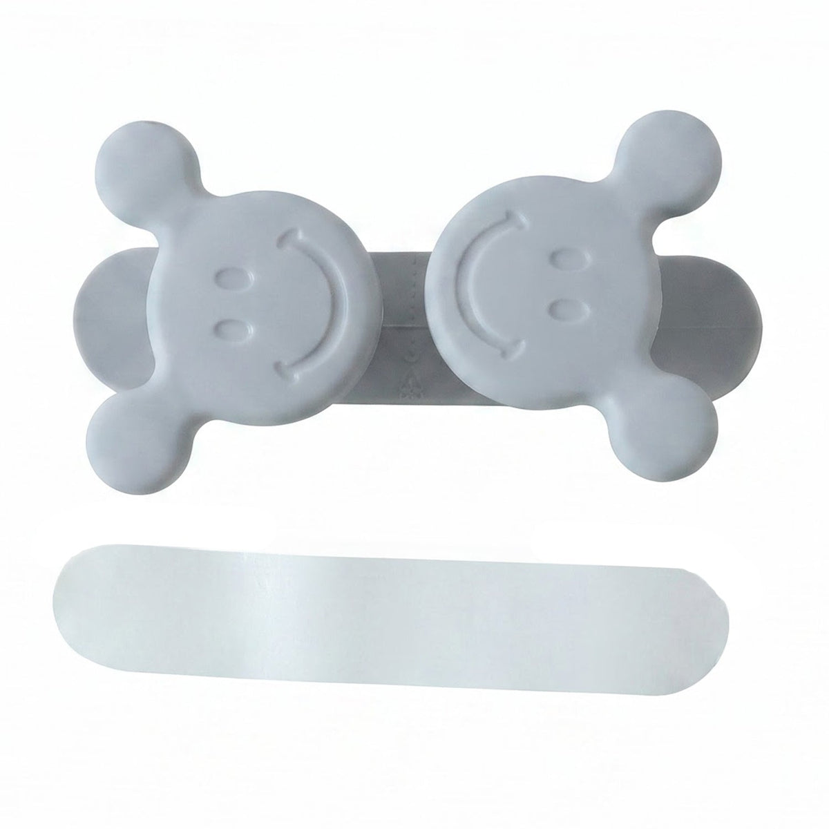 A gray silicone cord organizer with two smiling faces and a white adhesive strip on a white background.