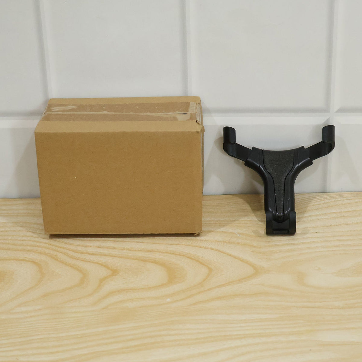 A brown cardboard box and a black gravity lock car phone holder resting on a light wooden floor against a white paneled wall.