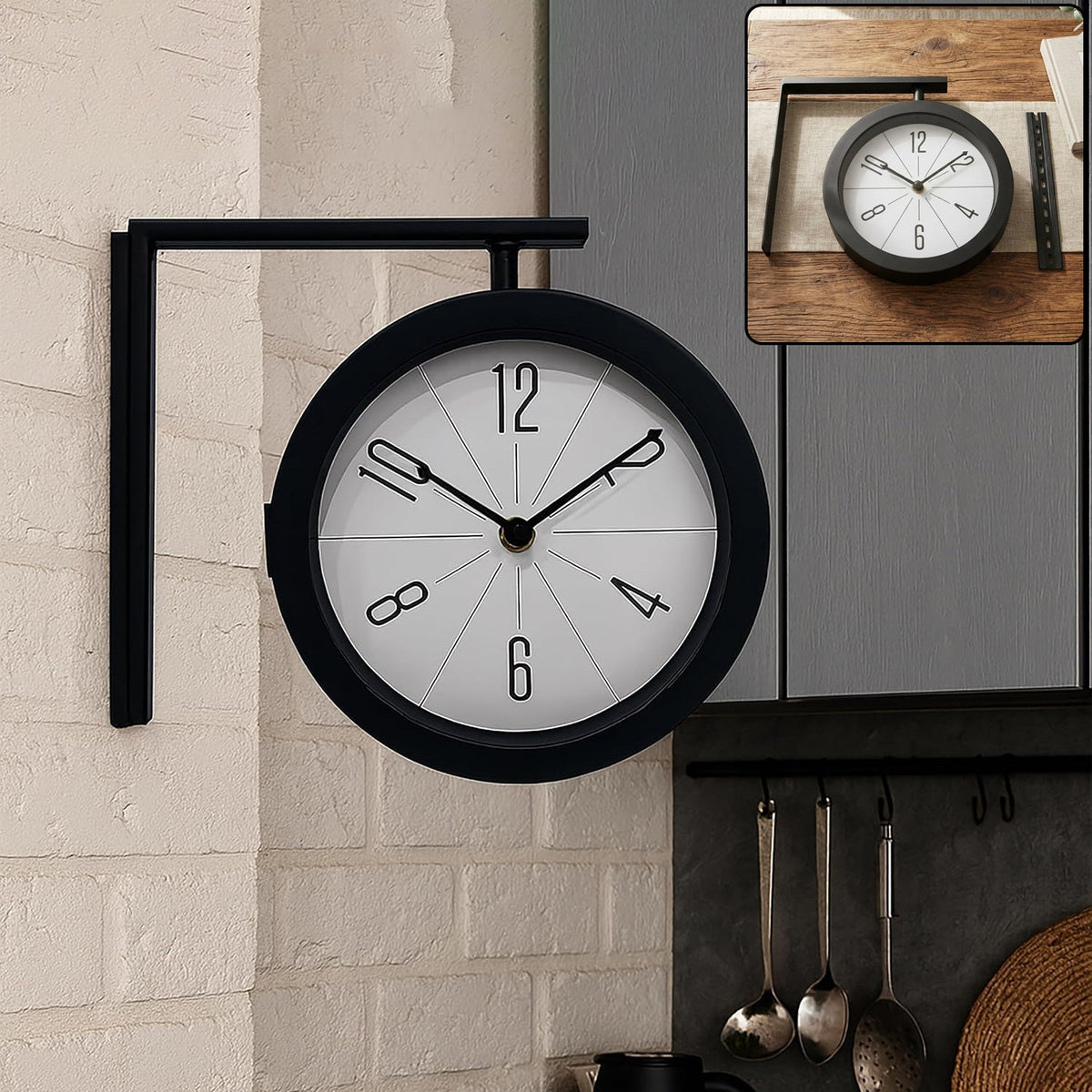A black double-sided wall clock with a white face and black numbers is mounted on a white brick wall in a kitchen setting. A