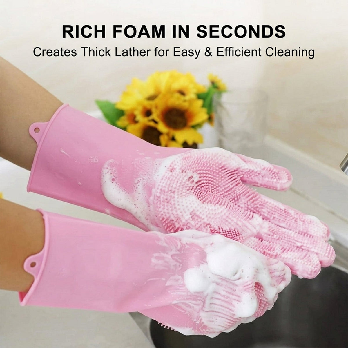 Close-up of hands in pink silicone scrubbing gloves, covered in rich white foam, with yellow flowers in the background.