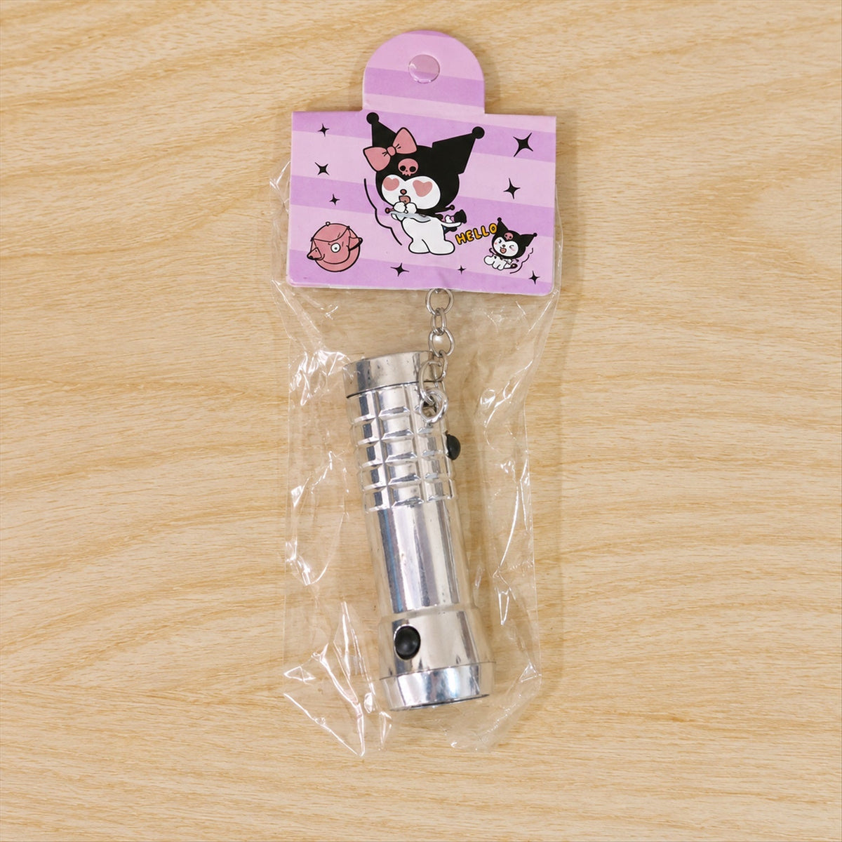 A silver keychain flashlight in clear plastic packaging with a purple cartoon-themed hang tag on a wooden surface.