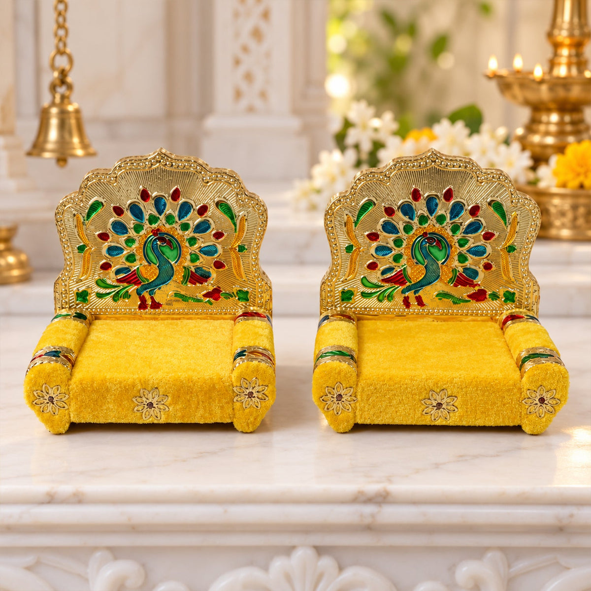 Two identical golden singhasans with yellow velvet seats and colorful peacock backrests, positioned on a white marble