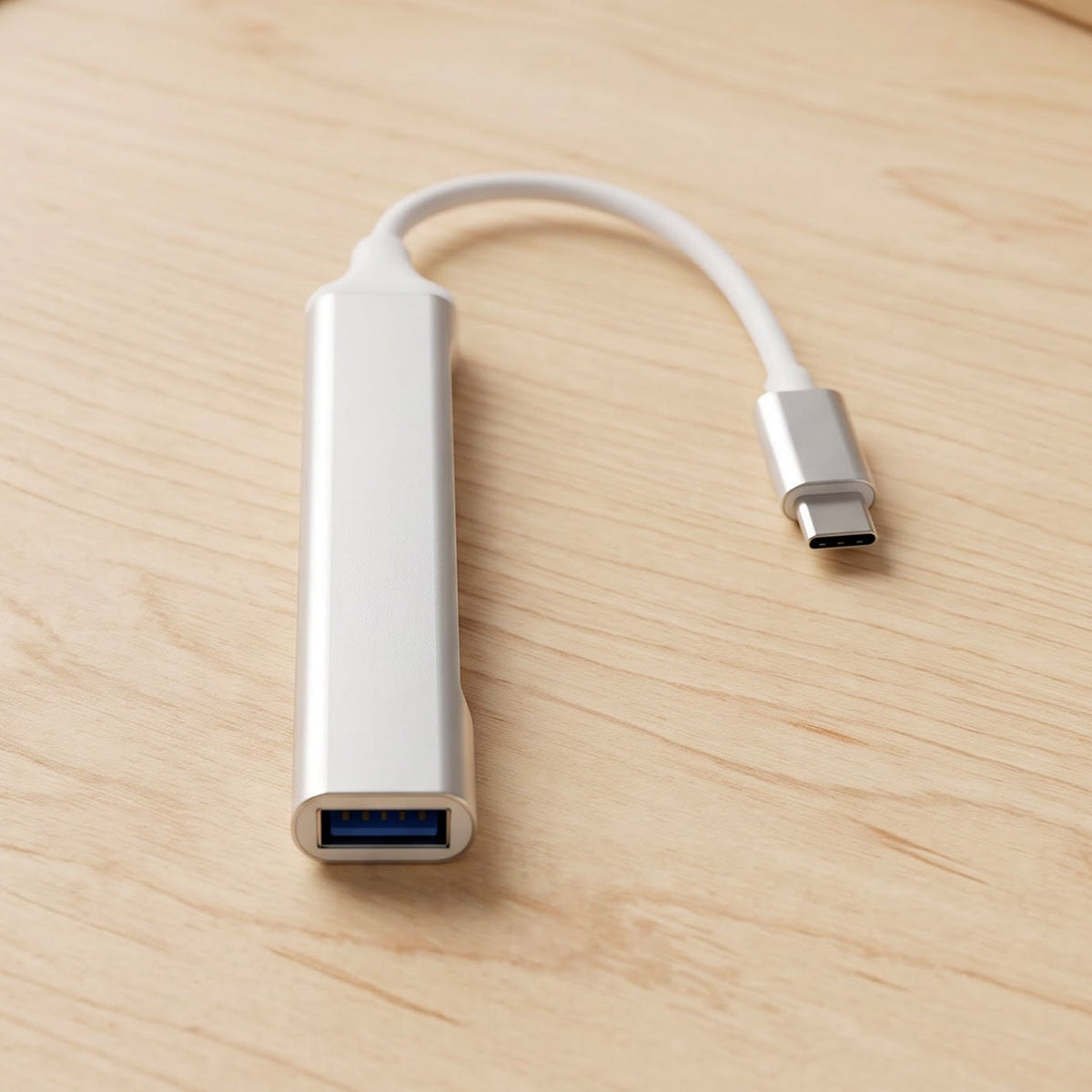 A silver Type C to four-port USB hub with a white cable and Type C connector resting on a light wooden surface.