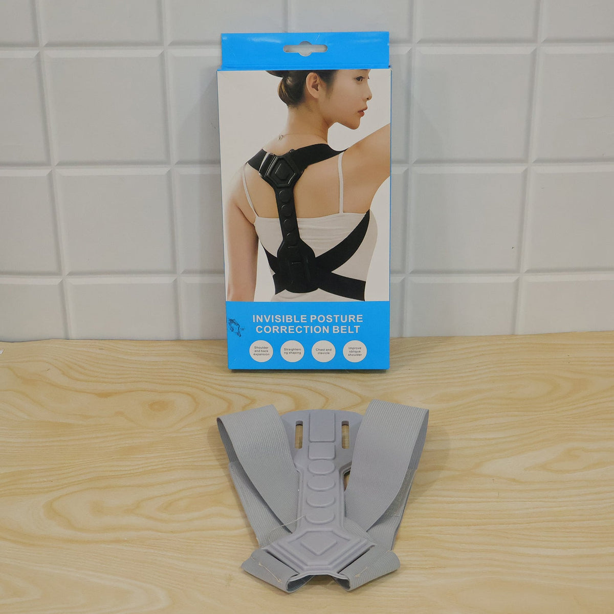 The gray posture corrector laid flat on a wooden surface in front of its blue and white product box.