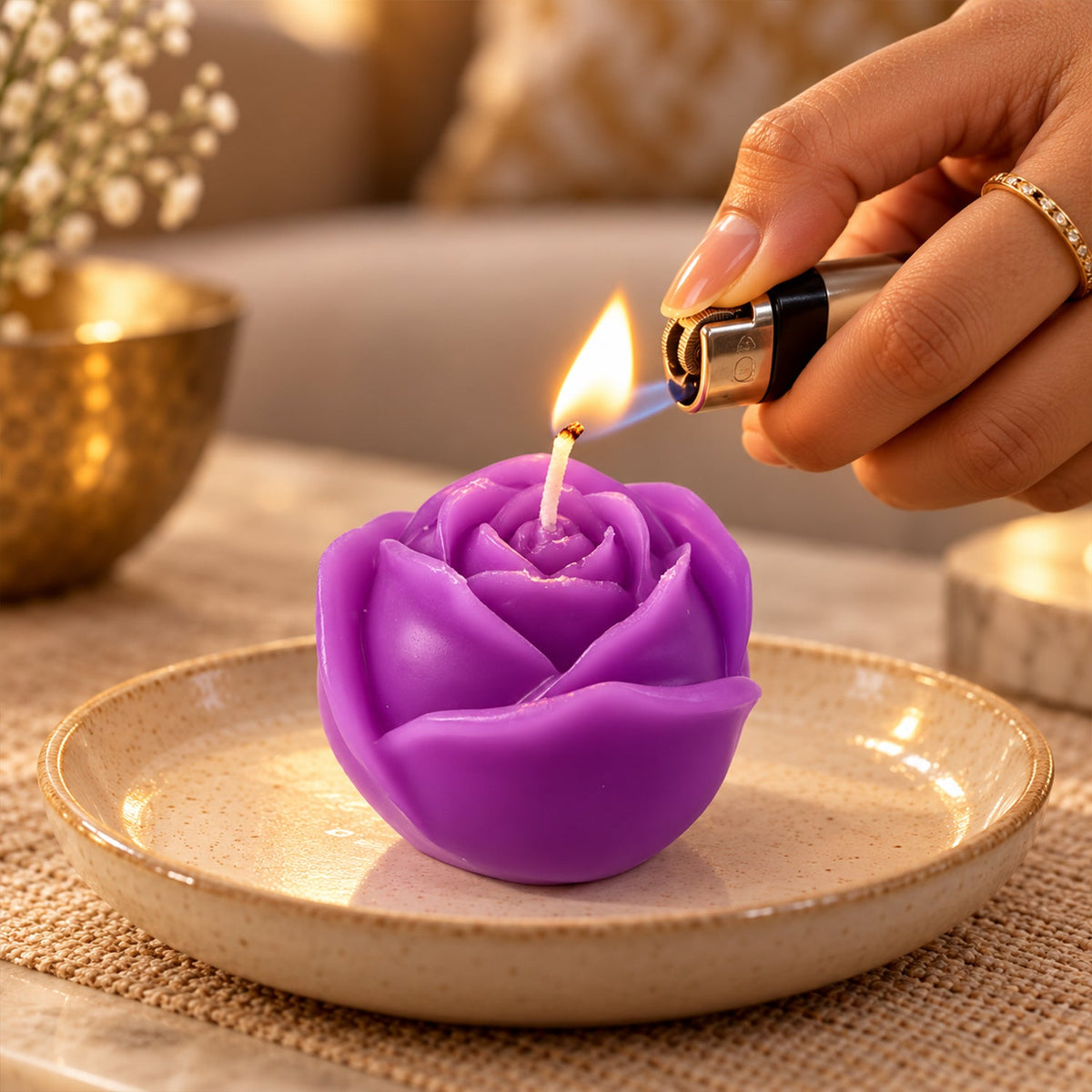A hand lights a purple rose-shaped candle on a textured plate using a black lighter, creating a warm glow.