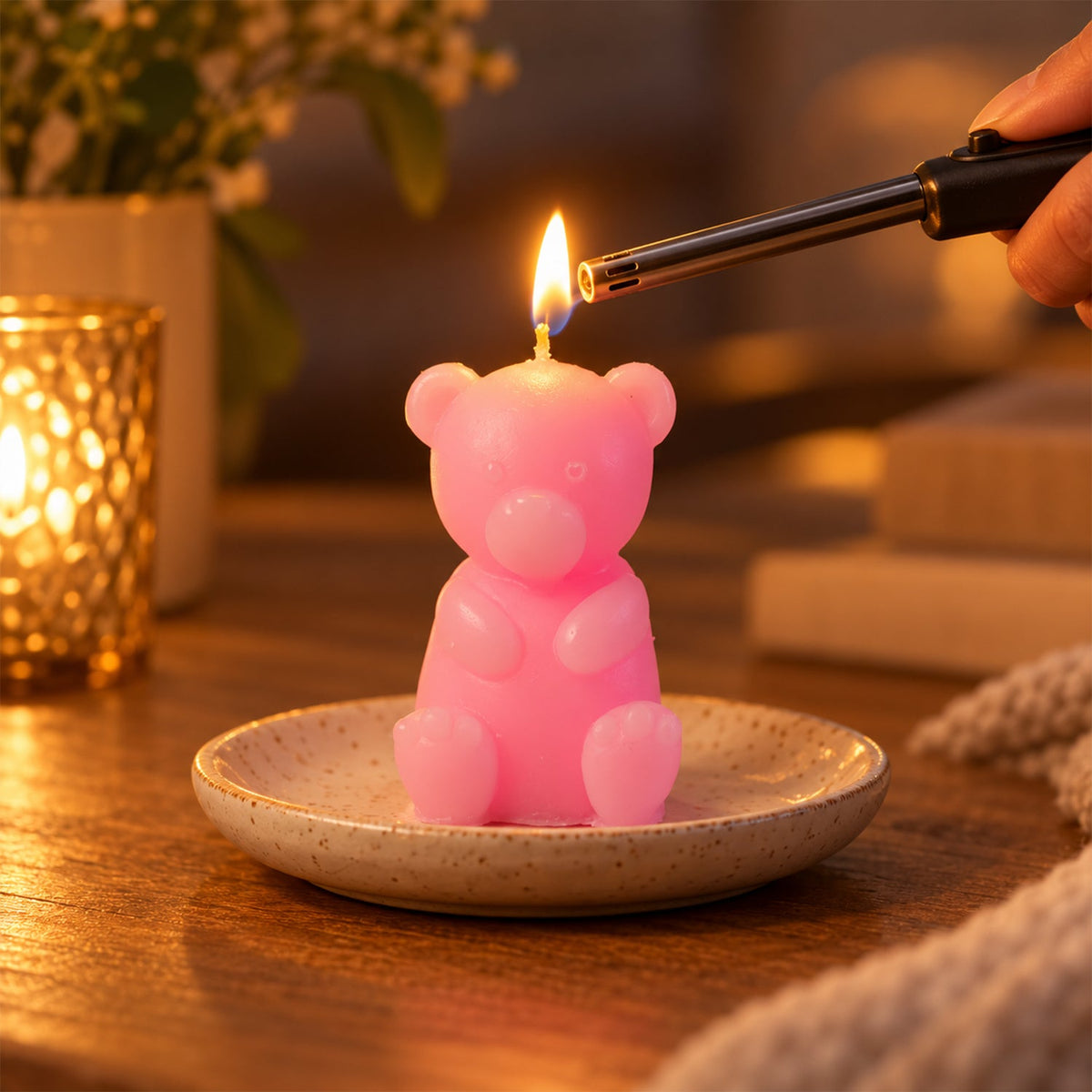 A hand lights a pink teddy bear candle on a ceramic plate with a long black lighter.