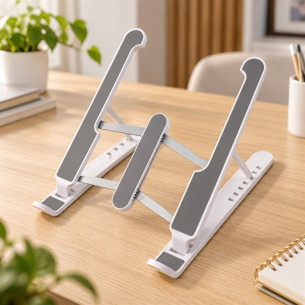 White and gray laptop stand with adjustable height and angle on a wooden desk with a plant.