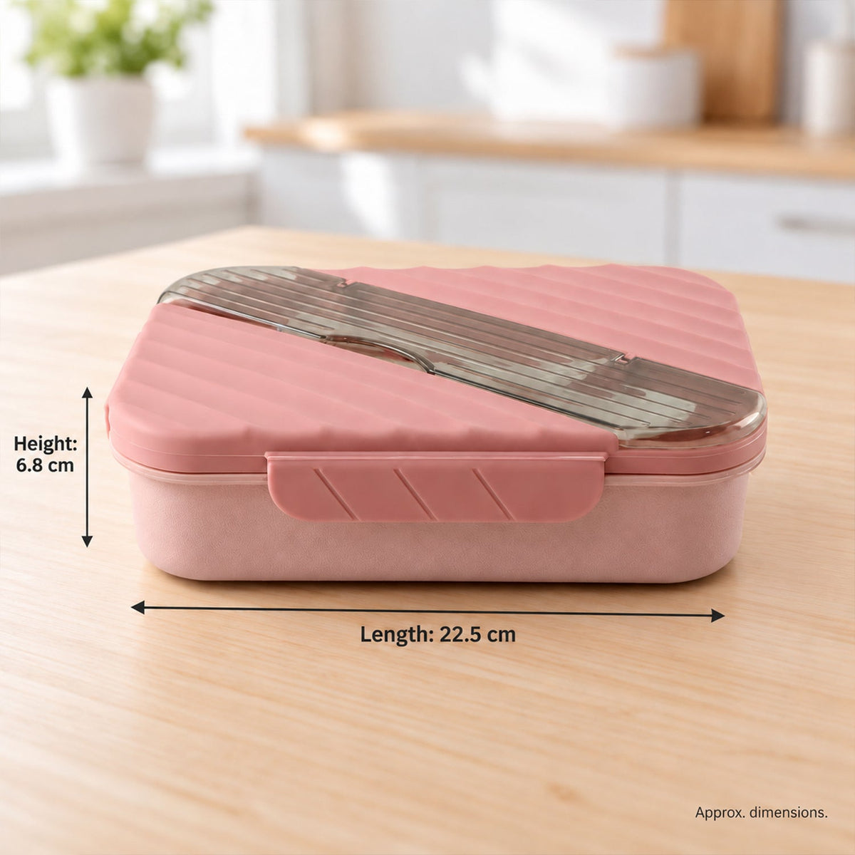 A pink lunchbox with a ribbed lid and clear cutlery section sits on a wooden table, displaying its length and height