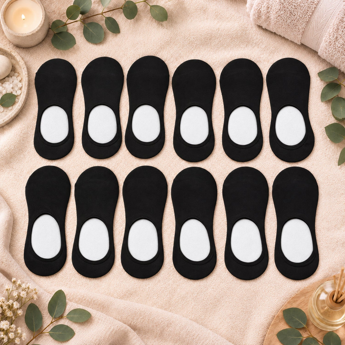 Twelve black low-cut socks with white heel grips, arranged on a beige towel with spa items.