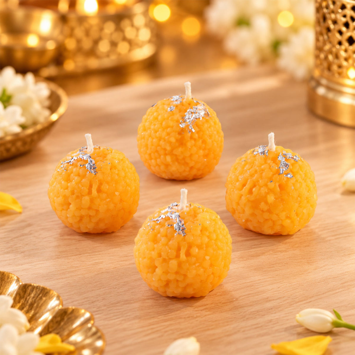 Four unlit orange spherical candles with silver flakes on a light wooden surface, with blurred decor.