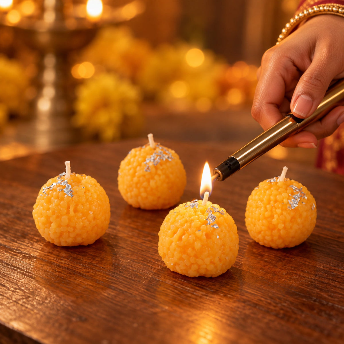 A hand lighting one of four orange spherical candles with silver flakes on a wooden surface.