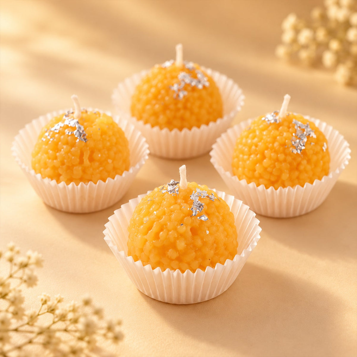 Four unlit orange spherical candles with silver flakes, each in a white cup, on a warm-toned surface.