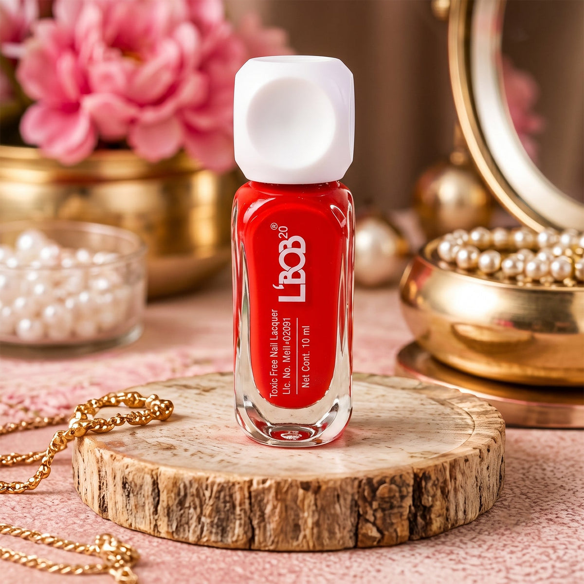 A red nail polish bottle with a white square cap sits on a wooden disc, surrounded by pearls and flowers.