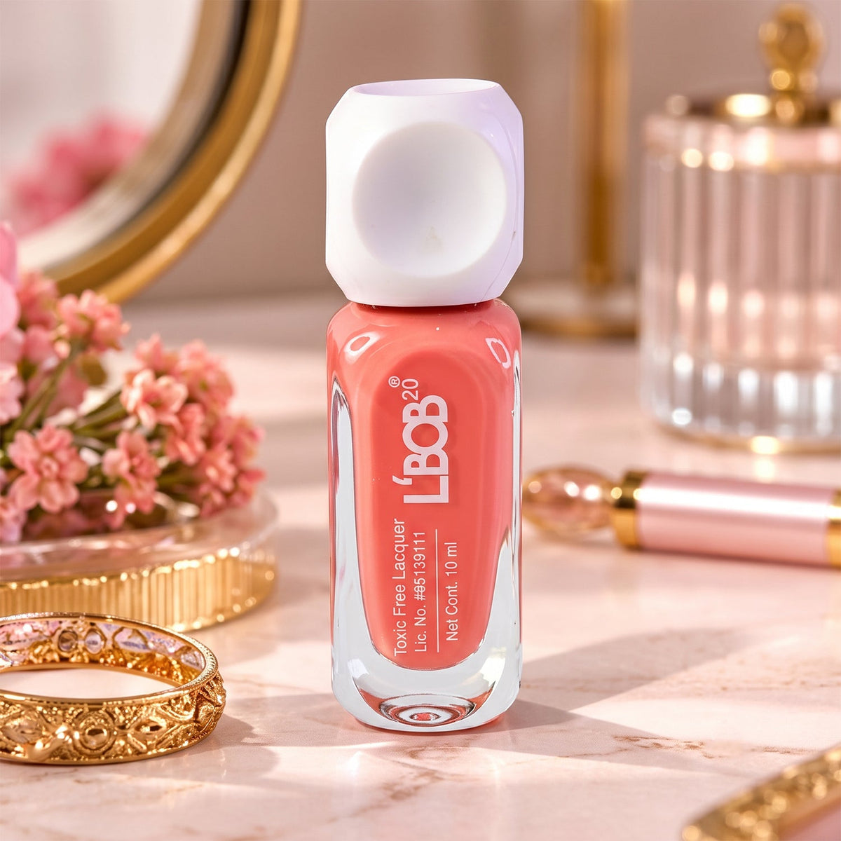 A small bottle of peach coral nail polish with a white dice-shaped cap sits on a marble surface next to a gold ring and pink
