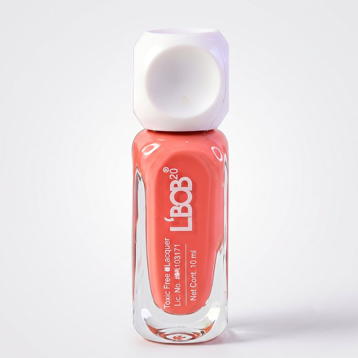 A single bottle of peach coral nail polish with a white dice-shaped cap stands upright on a plain white background.
