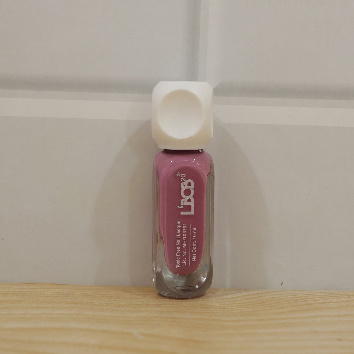Hand holding mauve rose colour nail polish bottle during manicure