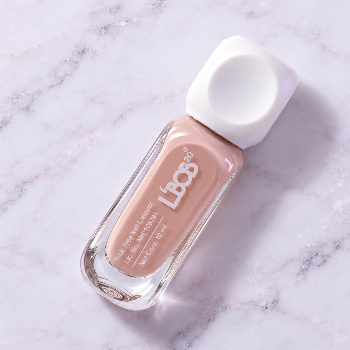 A bottle of nude pink nail polish with a white cap lies diagonally on a light grey marble surface.