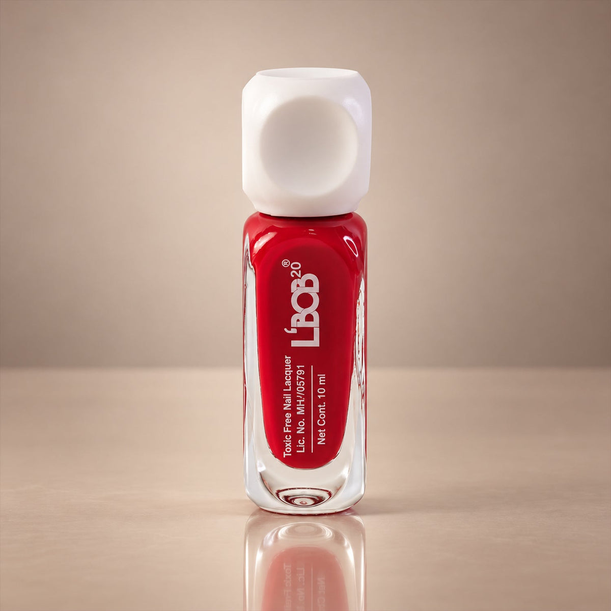 A bottle of red nail polish with a white cap stands on a reflective surface against a beige wall.