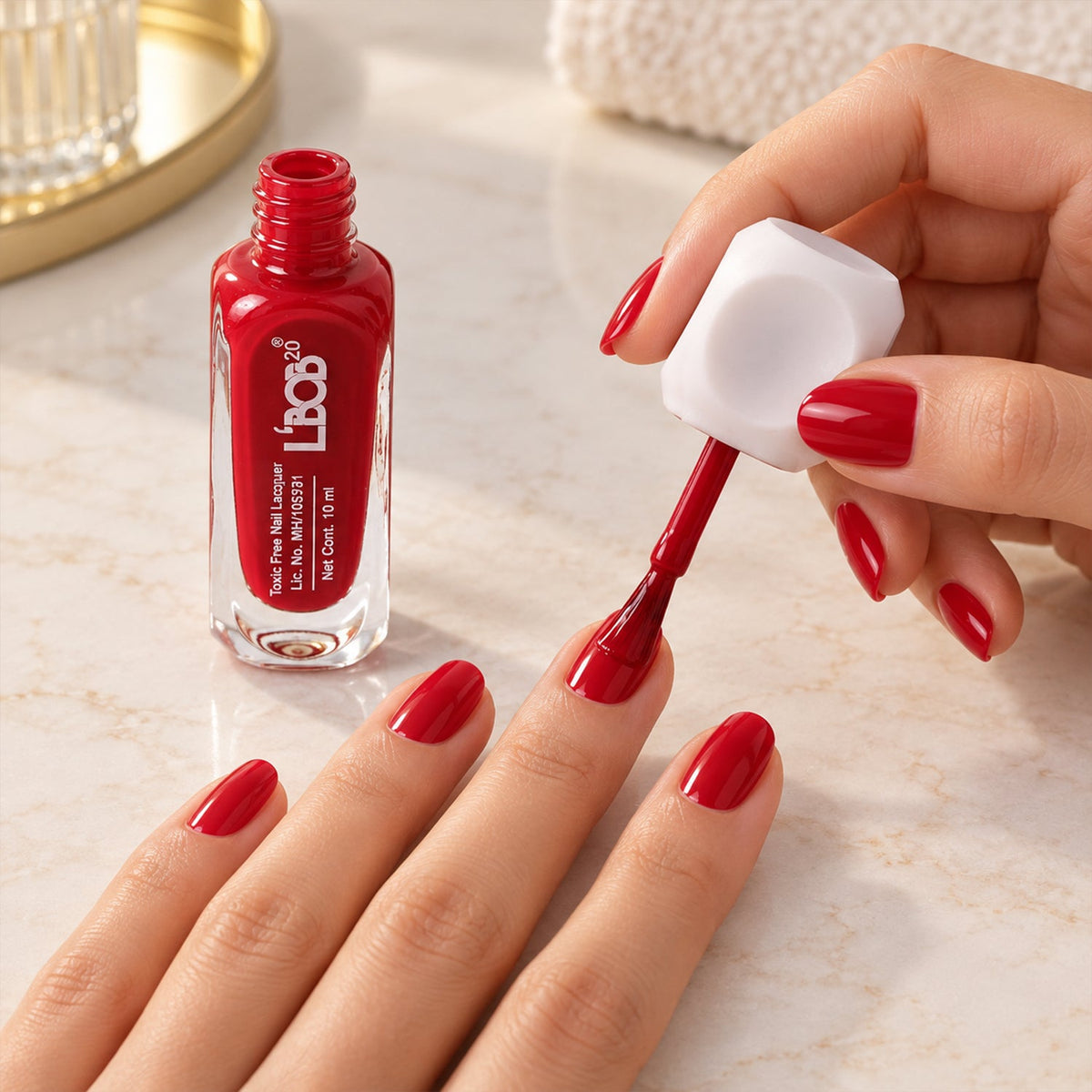 A person applies red nail polish to their left hand, with the open bottle visible on a marble surface.