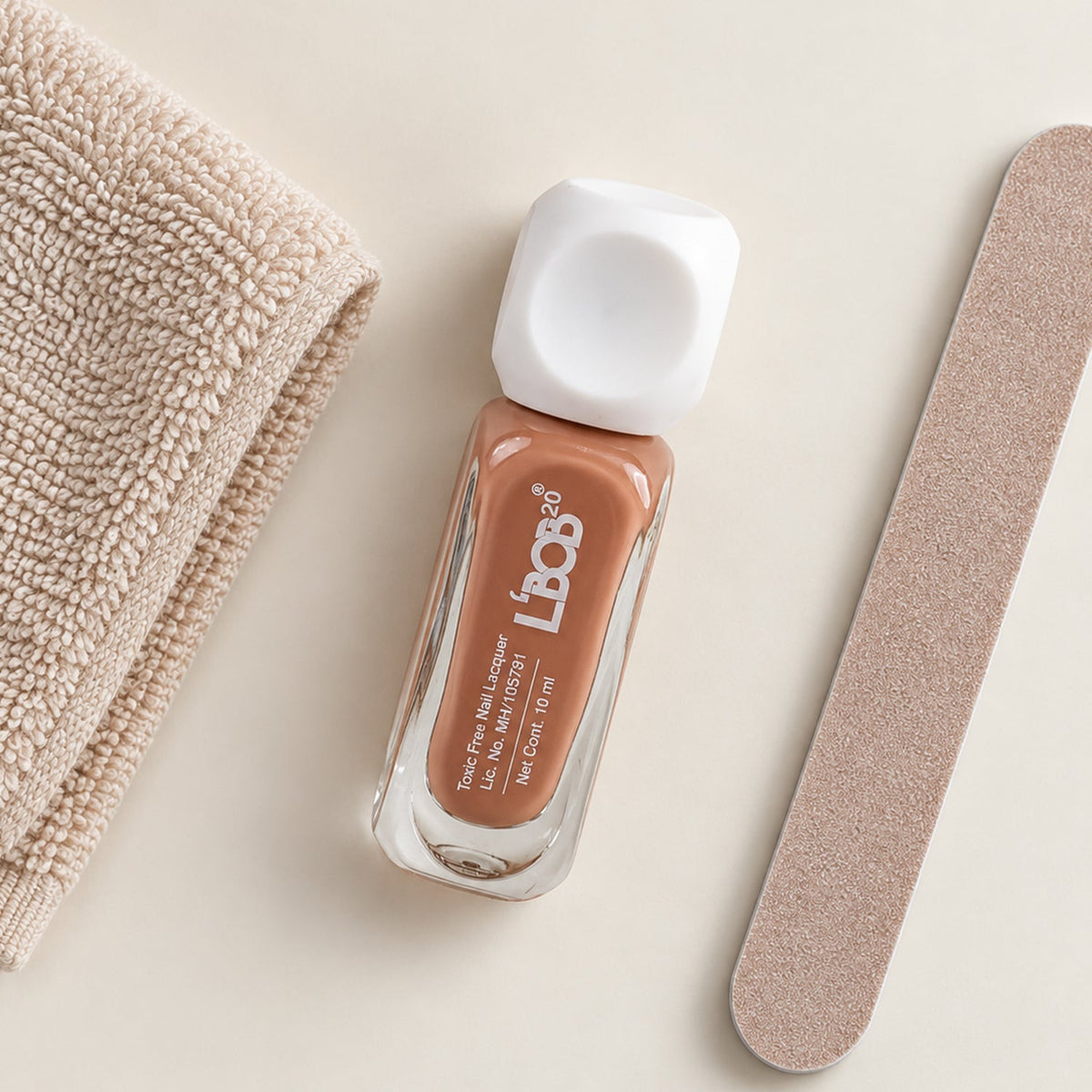 A small bottle of nude brown nail polish sits next to a beige towel and a nail file.