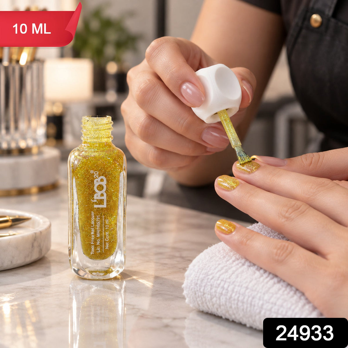 A person applies gold glitter nail polish to their fingernails with a brush, 10 ml bottle, product code 24933.