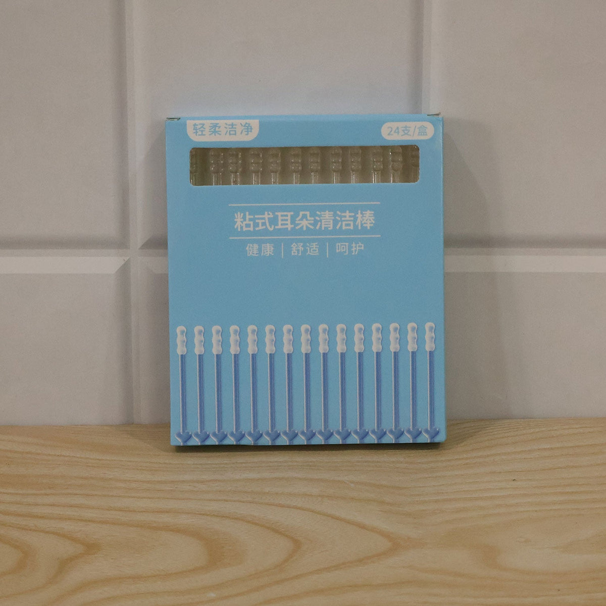 A light blue box of 24 ear cleaning sticks with Chinese text sits on a light wooden surface against a tiled wall.