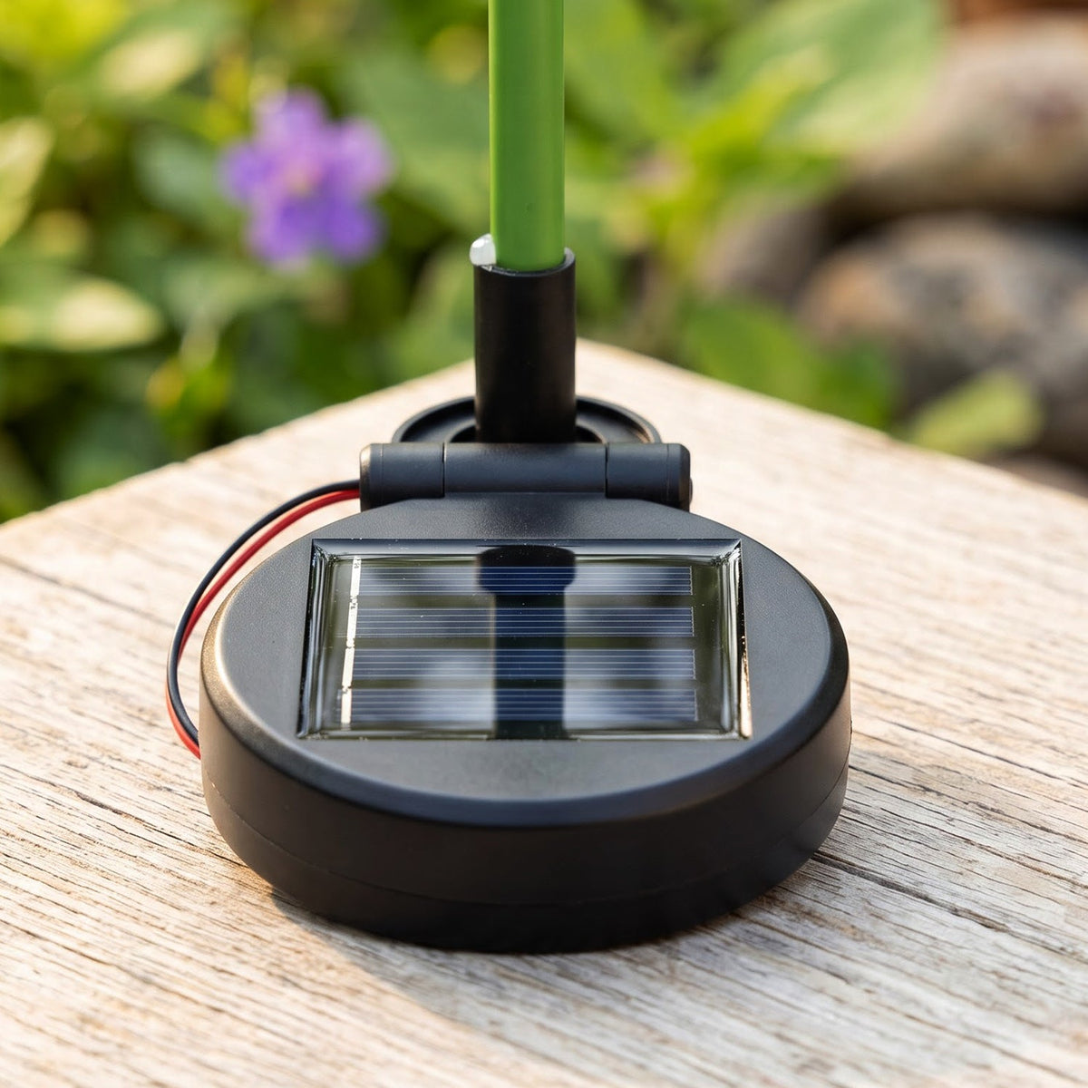 A close-up view of the black circular solar panel base of the flower stake light, resting on a wooden surface.