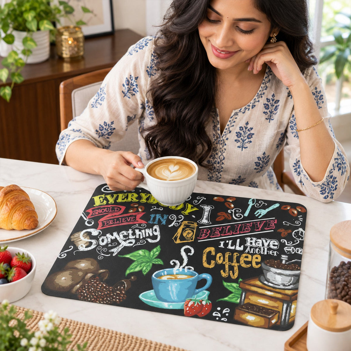 A woman smiles while holding a white coffee cup, with the coffee-themed mat on a light-colored table beside her.