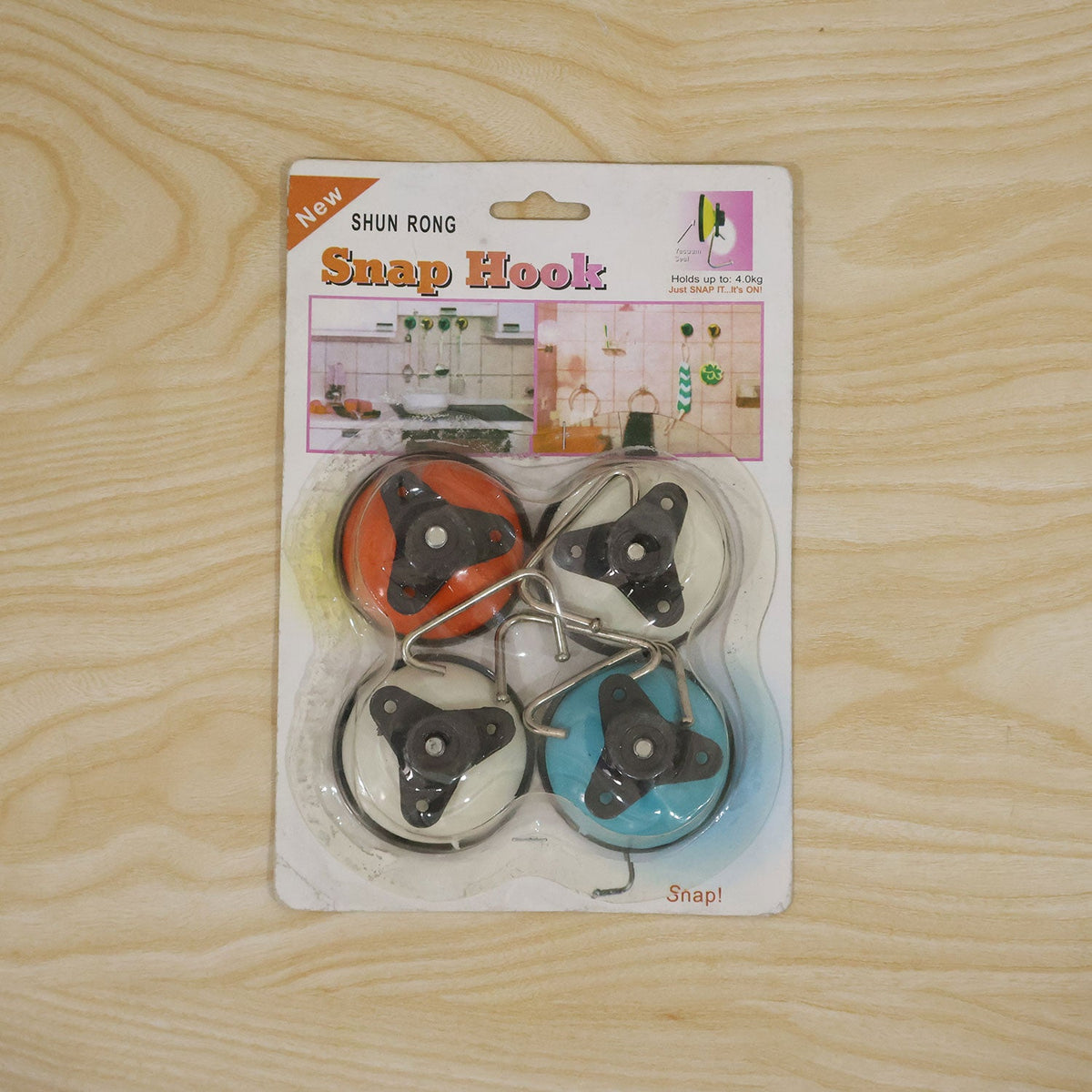 A retail package of four Shun Rong Snap Hooks in orange, white, and blue, lying flat on a light wooden surface.