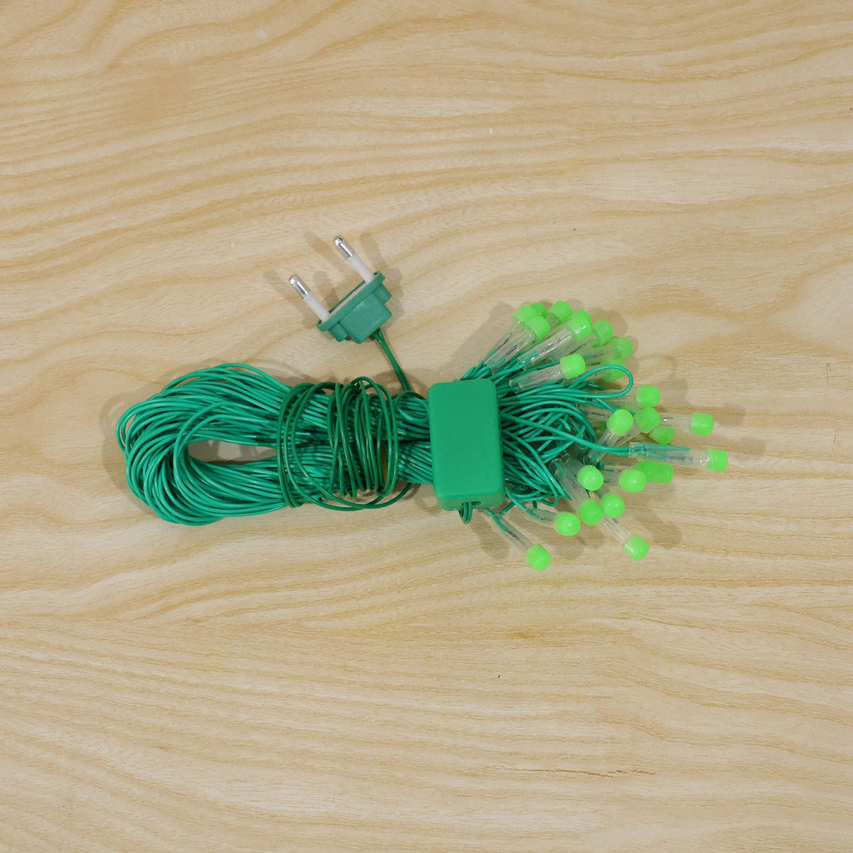 A coiled bundle of green LED string lights with a 2-pin plug and controller resting on a wooden surface.