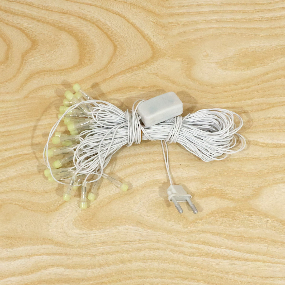 A coiled white LED string light set with clear bulbs and a power adapter, displayed on a light wooden surface.