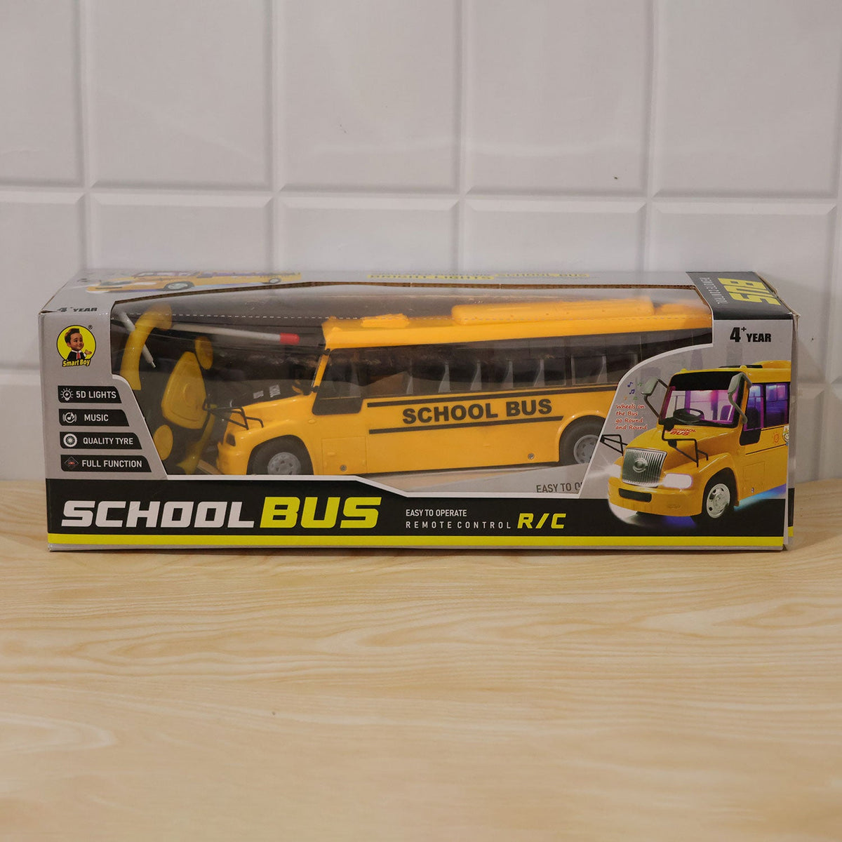 A yellow school bus toy displayed inside its clear plastic and cardboard packaging on a light wooden table.