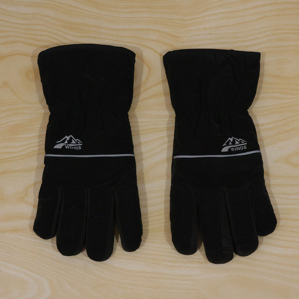 A pair of black winter gloves with white logos and reflective stripes, displayed on a light wooden surface.