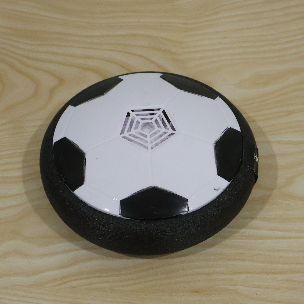 A white and black hoverball soccer toy with a textured foam edge rests on a light wooden surface.