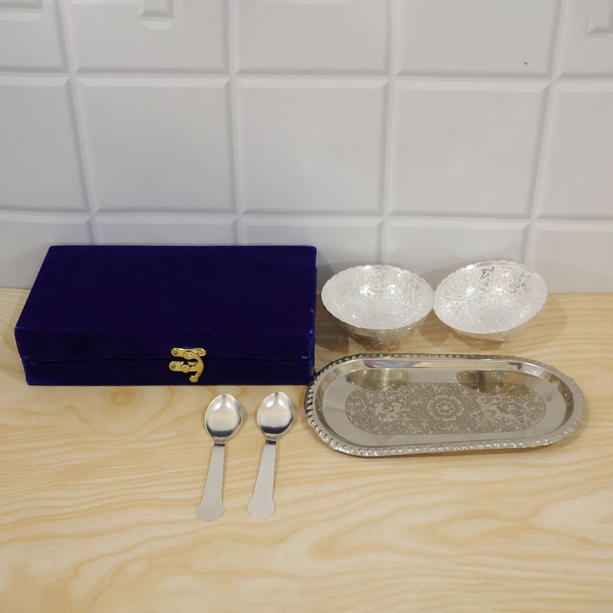 A silver-plated serving set, including two bowls, two spoons, an oval tray, and a blue velvet box, on a light wooden surface.