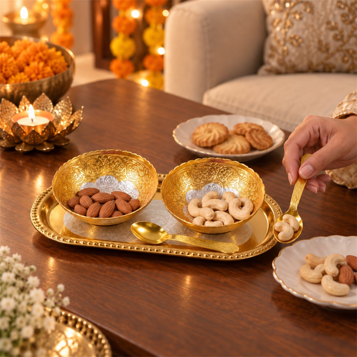 A person's hand holding a golden spoon with cashews, next to two golden bowls with nuts on a tray.